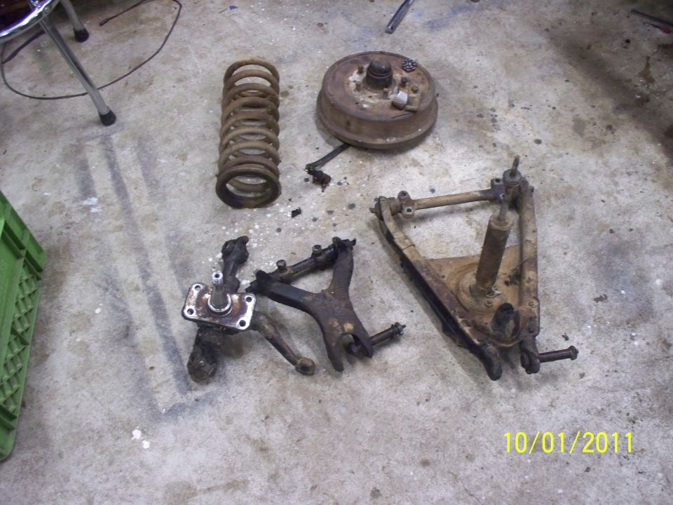 Rusty car suspension parts including a coil spring, brake drum, and control arms on a concrete floor