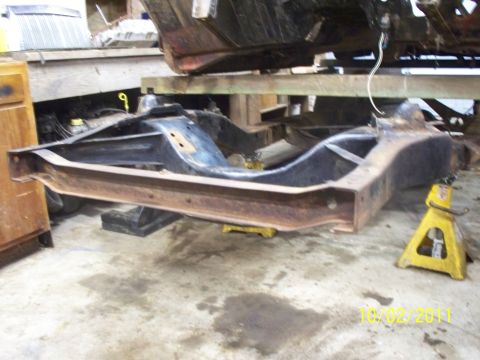 1990 Ford Bronco - The frame of a vehicle is supported by jack stands in a workshop, with a date stamp visible in the lower right corner.