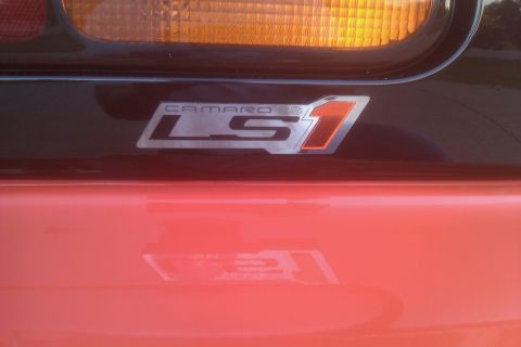 1999 Chevrolet Camaro - Close-up of a 'Camaro LS1' badge on the rear of a red vehicle.