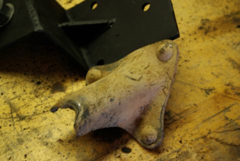 1995 Ford Bronco - A close-up view of a worn suspension bracket and a black metal bracket resting on a wooden surface.