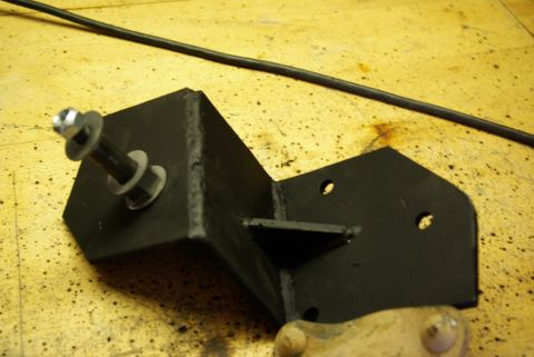 1995 Ford Bronco - A close-up view of a metal bracket with hardware, resting on a workbench surface.