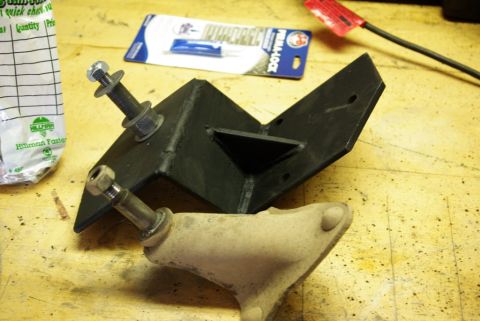 1995 Ford Bronco - A black metal bracket and a beige suspension part are laid out on a wooden surface, possibly for installation.