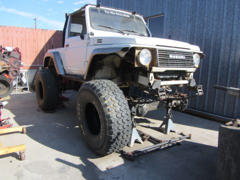 1987 Suzuki Samurai - A white 1987 Suzuki Samurai is shown on jack stands, large off-road tires and a modified front end.