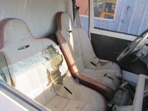 1987 Suzuki Samurai - The interior of a vehicle shows worn racing seats and a steering wheel, with visible text on the driver's seat.