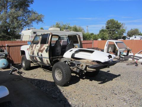 1987 Suzuki Samurai - A partially disassembled pickup truck with camouflage paint sits in a yard next to another vehicle.