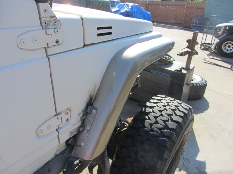 1987 Suzuki Samurai - Side view of a white Suzuki Samurai showing its fender and door hinge, with a large off-road tire visible.