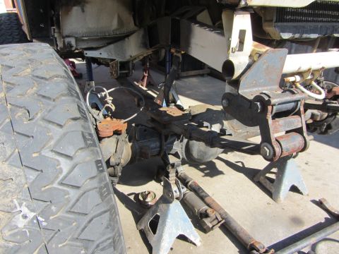 1987 Suzuki Samurai - The underside of a vehicle is shown on jack stands, revealing its suspension and drivetrain components.