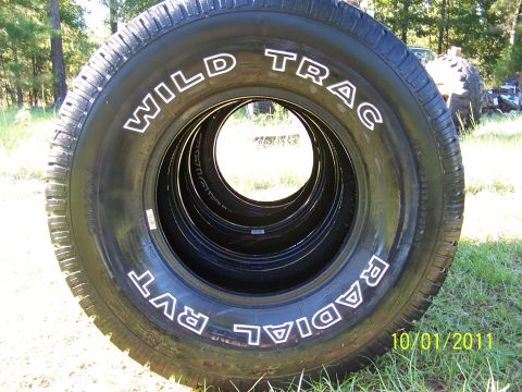 1986 Ford Bronco - A stack of tires with 'WILD TRAC RADIAL RVT' written on them is shown outdoors.
