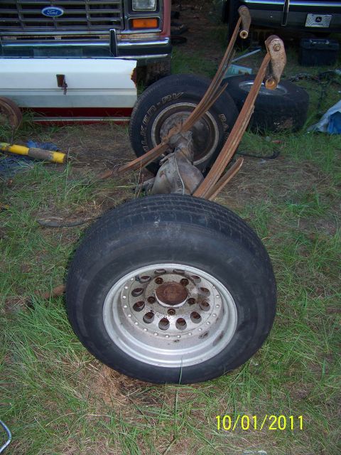 1986 Ford Bronco - Rear axle assembly with leaf springs and tires, possibly from a 1986 Ford Bronco, sits on the grass.