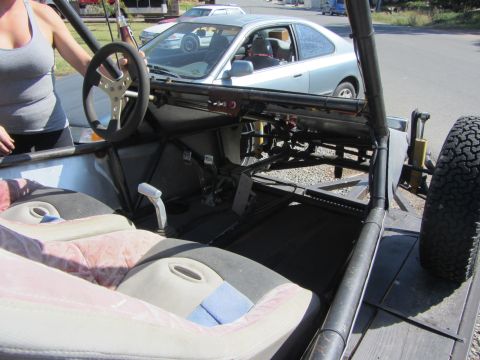 1987 Suzuki Samurai - Interior view of a custom off-road buggy, showing the roll cage and seats. A sedan is parked behind it.