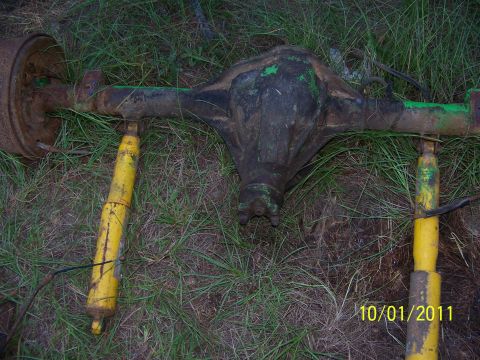 1986 Ford Bronco - A Dana 60 axle with two yellow shock absorbers is visible, lying on the ground amidst grass and dirt.