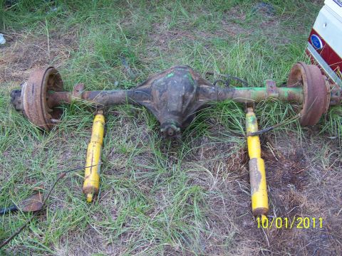 1986 Ford Bronco - A rear axle assembly, likely from a Ford truck or SUV, rests on the ground with two yellow shock absorbers attached.