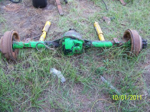 1986 Ford Bronco - A green Dana 60 axle assembly with yellow shocks and rusty brake drums lies on the grass.