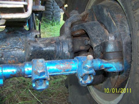 1986 Ford Bronco - Detail of a vehicle's front axle and steering linkage, showing wear and aftermarket blue paint.