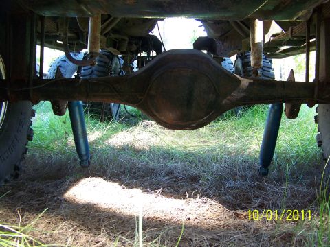 1986 Ford Bronco - Underside view of a vehicle's rear axle and suspension system, with grass and dirt visible below.