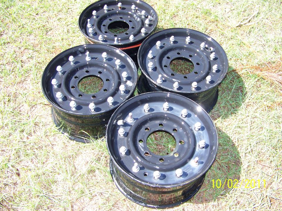 four black steel wheels with lug nuts on grass