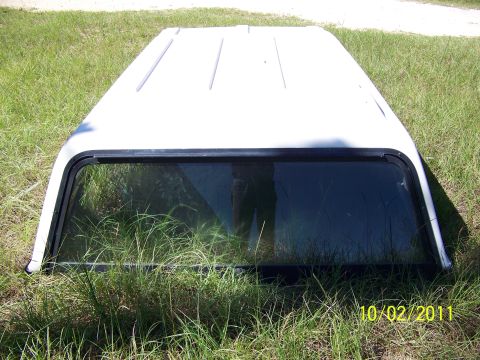 1986 Ford Bronco - A white truck topper with a tinted window is shown resting on grass.