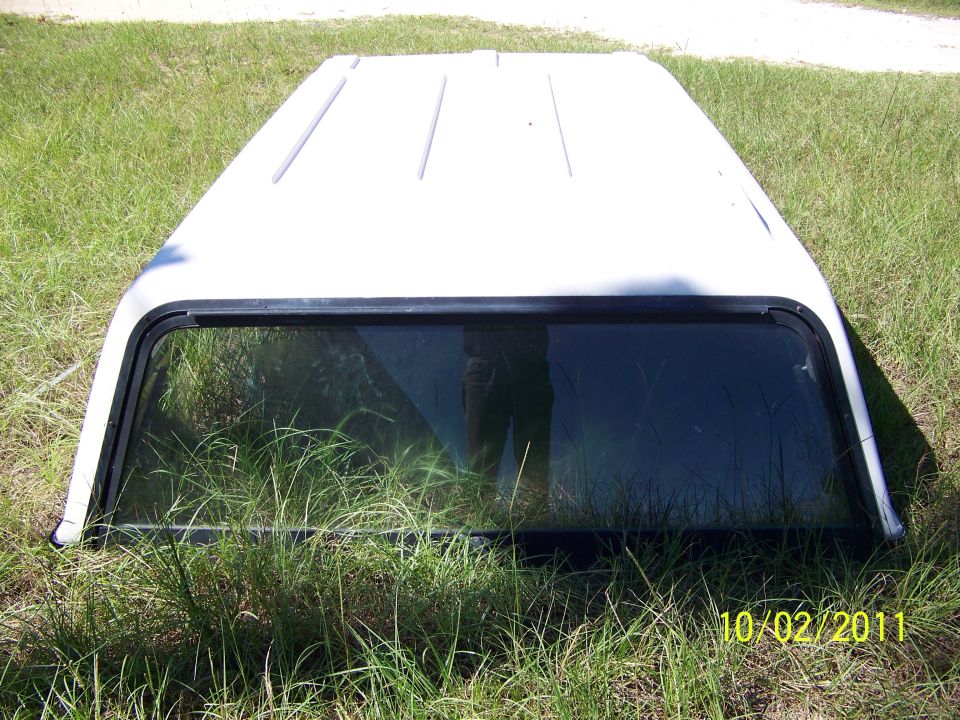 White truck topper with a tinted window lying on grass
