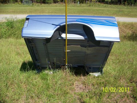 1986 Ford Bronco - A detached blue pickup truck bed with graphic stripes is resting on the grass next to a road.