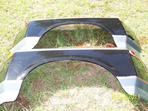 1986 Ford Bronco - Two vehicle fenders are shown resting on the grass, with a watermark indicating the photo was taken in 2011.