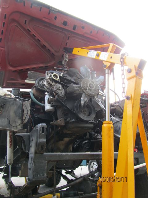 1984 Ford Bronco - Engine removal in progress, with a yellow engine crane lifting the power plant from a red vehicle.