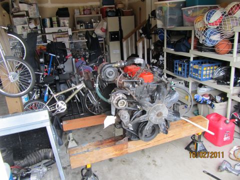 1984 Ford Bronco - Engine assembly with turbocharger and fan sits on a wooden stand in a cluttered garage.