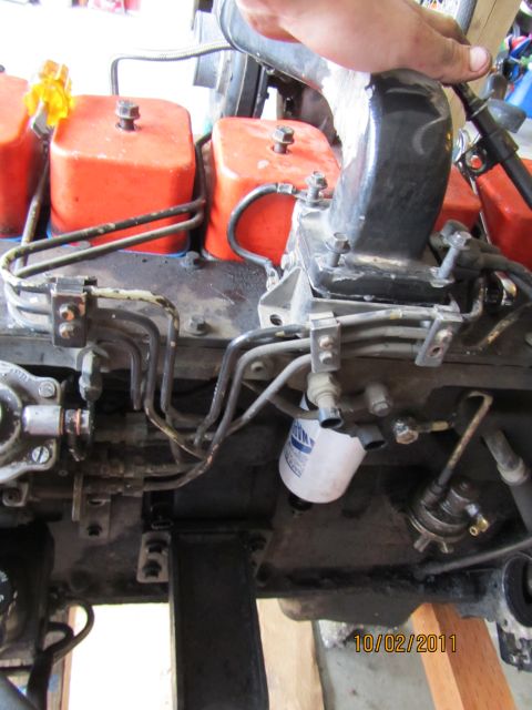 1984 Ford Bronco - Close-up view of engine components, including fuel filters and intake manifold, with a hand visible.