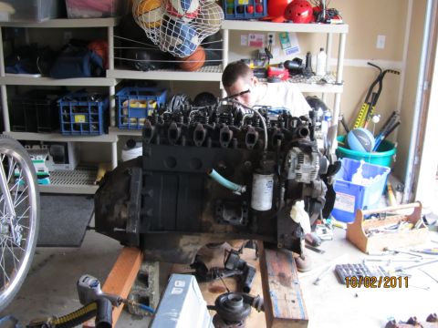 1984 Ford Bronco - A person works on a large diesel engine that is mounted on a stand in a garage setting.