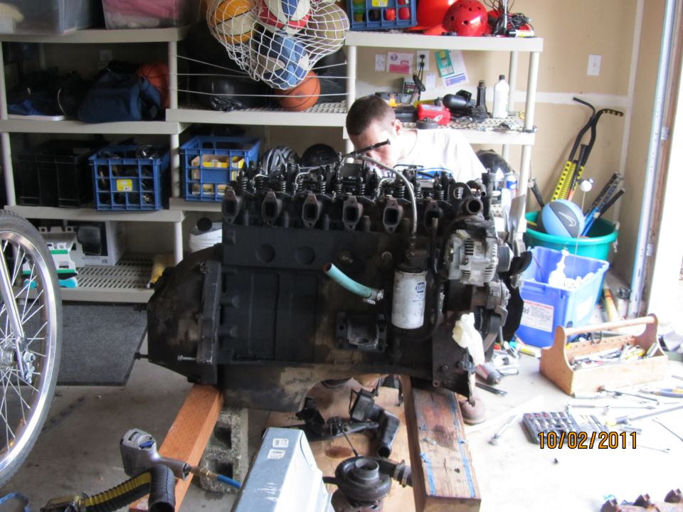 diesel engine on wooden stand in garage, person working on it