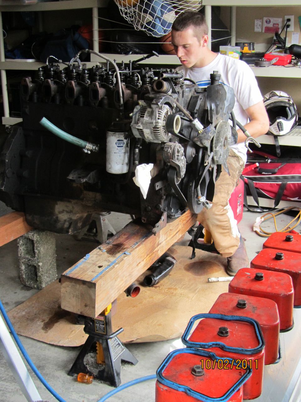Engine on stands with a person working on it, red fuel cans in foreground