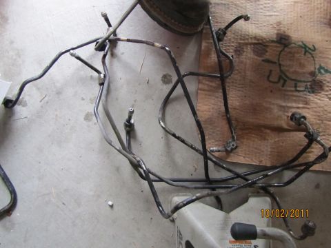 1984 Ford Bronco - Metal brake lines are shown on a concrete floor, possibly for a vehicle repair.