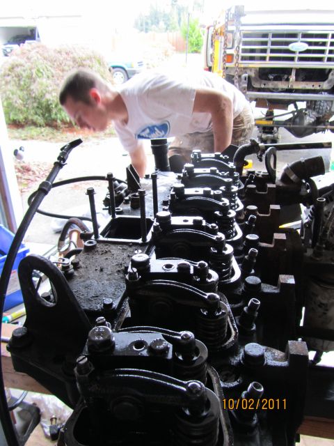 1984 Ford Bronco - A man inspects an engine block, with the front of a truck visible in the background.