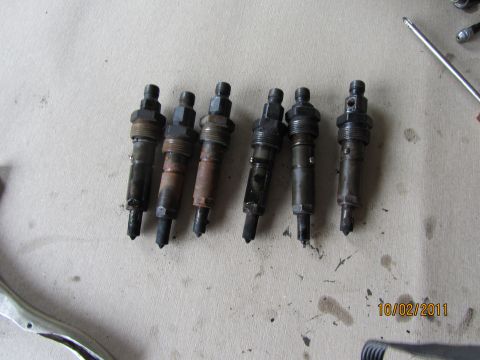 1984 Ford Bronco - Six diesel fuel injectors are shown on a workbench. A screwdriver is also visible in the image.