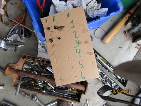 1984 Ford Bronco - A cardboard sheet with numbered bolts is laid out on the ground next to a collection of tools.