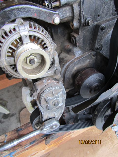1984 Ford Bronco - Close-up of an engine's alternator and belt tensioner assembly, with a tool attached.