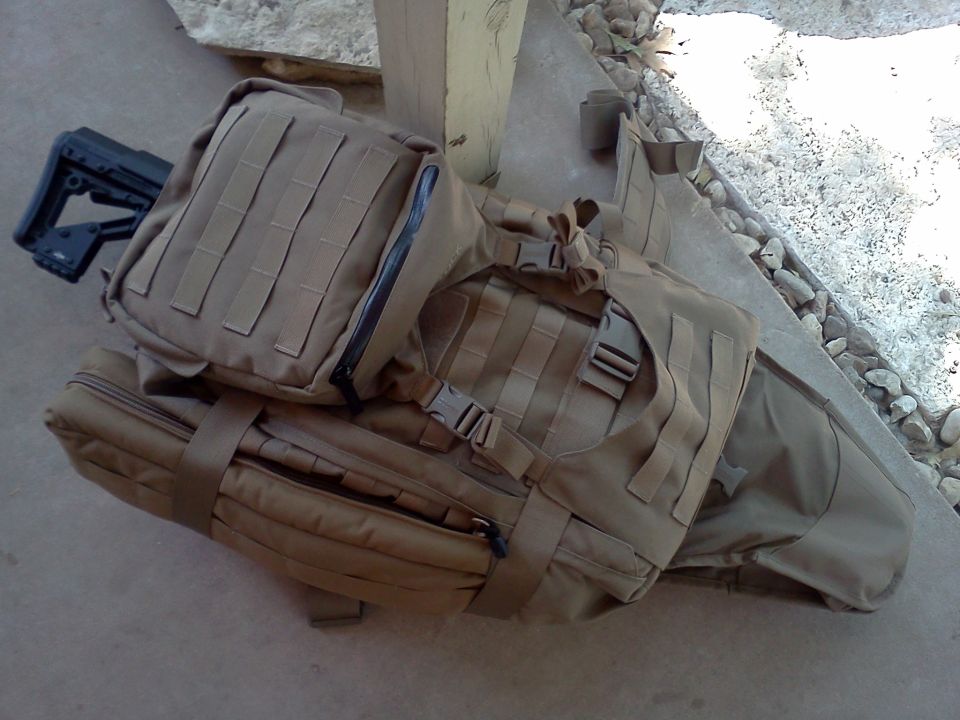 Tan tactical bags and a rifle stock are piled on the ground