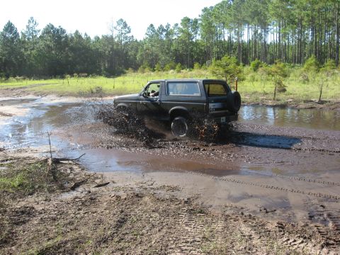 1994 Ford Bronco - Ford Bronco navigates a challenging muddy terrain, kicking up a large spray.