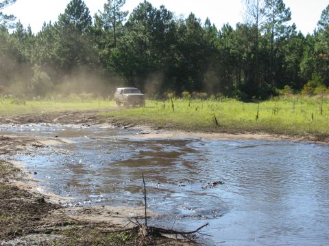 1994 Ford Bronco - A 1994 Ford Bronco navigates a muddy terrain, creating a dust cloud behind it.
