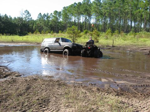 1994 Ford Bronco - An ATV pulls a stuck Ford Bronco out of a muddy mire surrounded by trees.