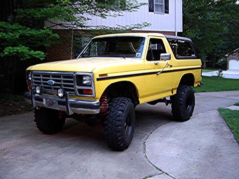 1985 Ford Bronco - This lifted Ford Bronco sits on a driveway, its bright yellow paint contrasting with the dark tires and black trim.