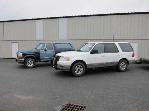1991 Ford LTD Crown Victoria - Two Ford vehicles, an Expedition and a Bronco, are parked side-by-side in front of a large industrial building.