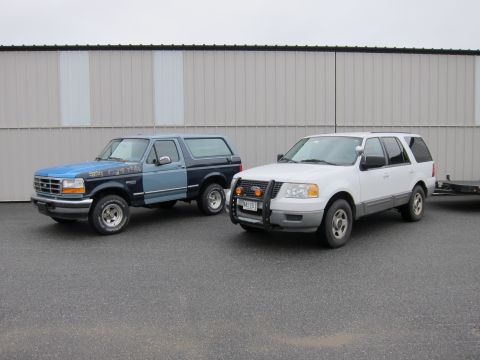 1991 Ford LTD Crown Victoria - A blue and dark blue Ford Bronco and a white Ford Expedition are parked next to each other in front of a building.