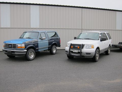 1991 Ford LTD Crown Victoria - Two SUVs are parked side-by-side in front of a large industrial building.