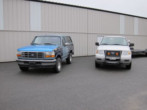 1991 Ford LTD Crown Victoria - Two Ford trucks, a Bronco and an F-150, are parked outside a building.