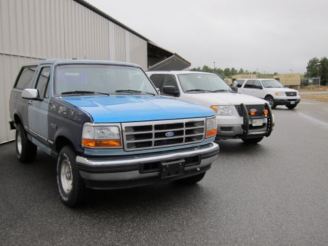 1991 Ford LTD Crown Victoria - Three Ford SUVs are parked in a line on a wet asphalt surface in front of a building.