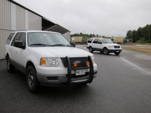 1991 Ford LTD Crown Victoria - Two white Ford Expeditions are parked outside a large building on a cloudy day.