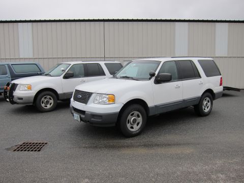 1991 Ford LTD Crown Victoria - Two white Ford Expeditions are parked in front of a commercial building.