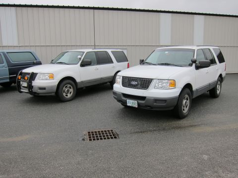 1991 Ford LTD Crown Victoria - Two white Ford Expedition SUVs are parked in front of a large building.