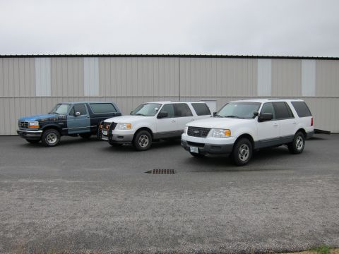 1991 Ford LTD Crown Victoria - Three white SUVs are parked in front of a large building, with a two-tone SUV to their left.