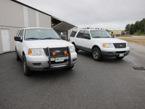 1991 Ford LTD Crown Victoria - Two white Ford Expeditions parked outside a building. The front one has a bull bar and auxiliary lights.
